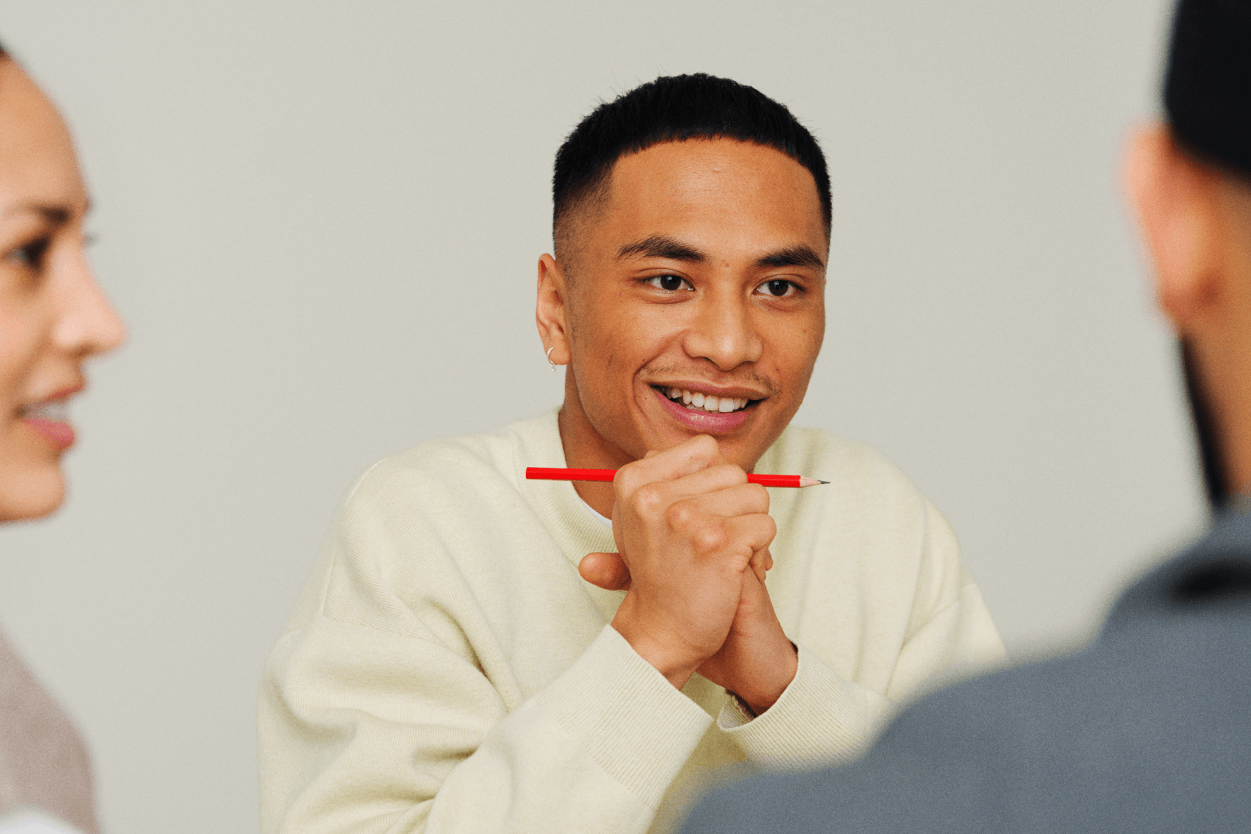 Person smiling and holding a red pen while engaged in a group conversation.