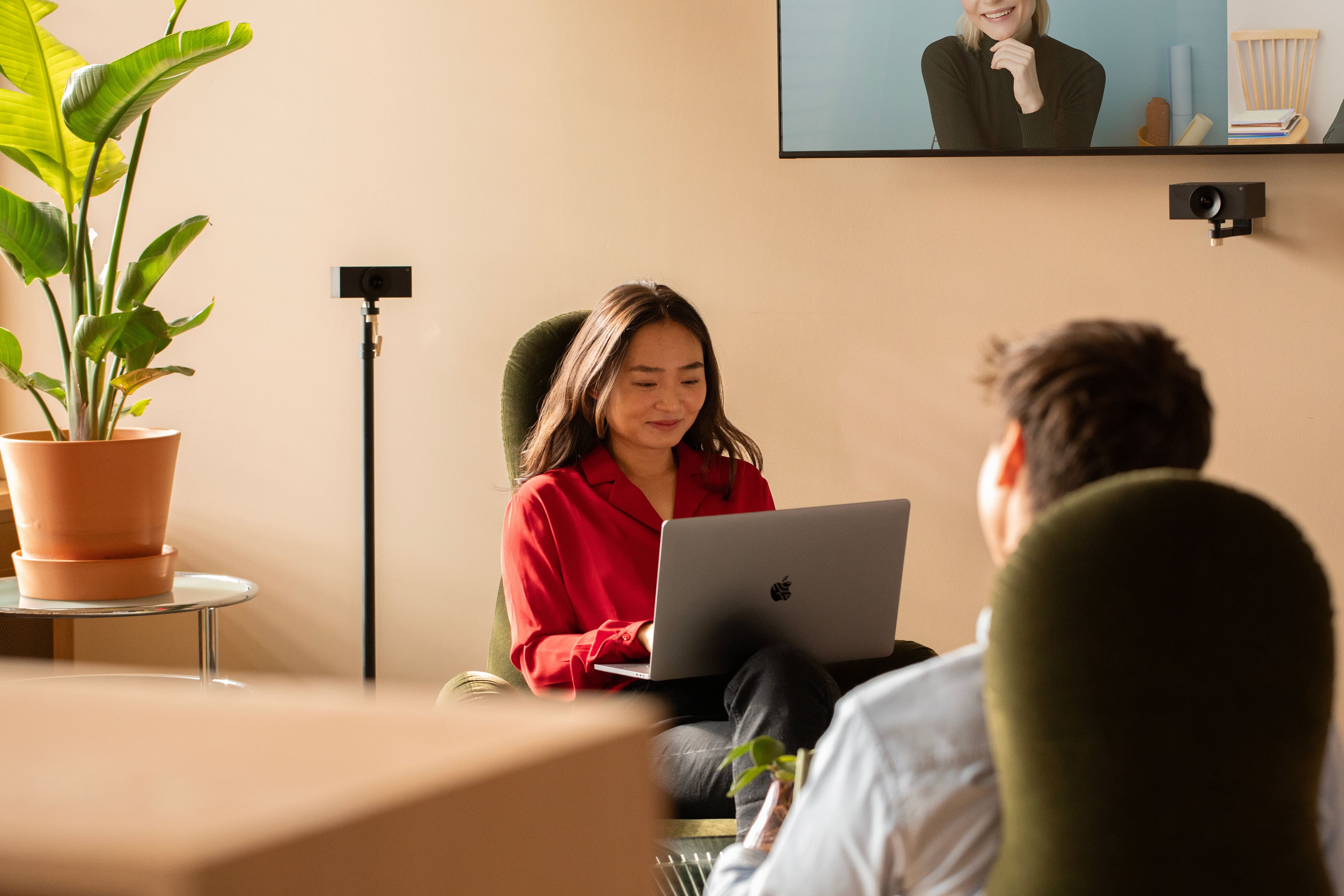 Woman using a laptop during a video meeting, with colleagues present in person and on screen.